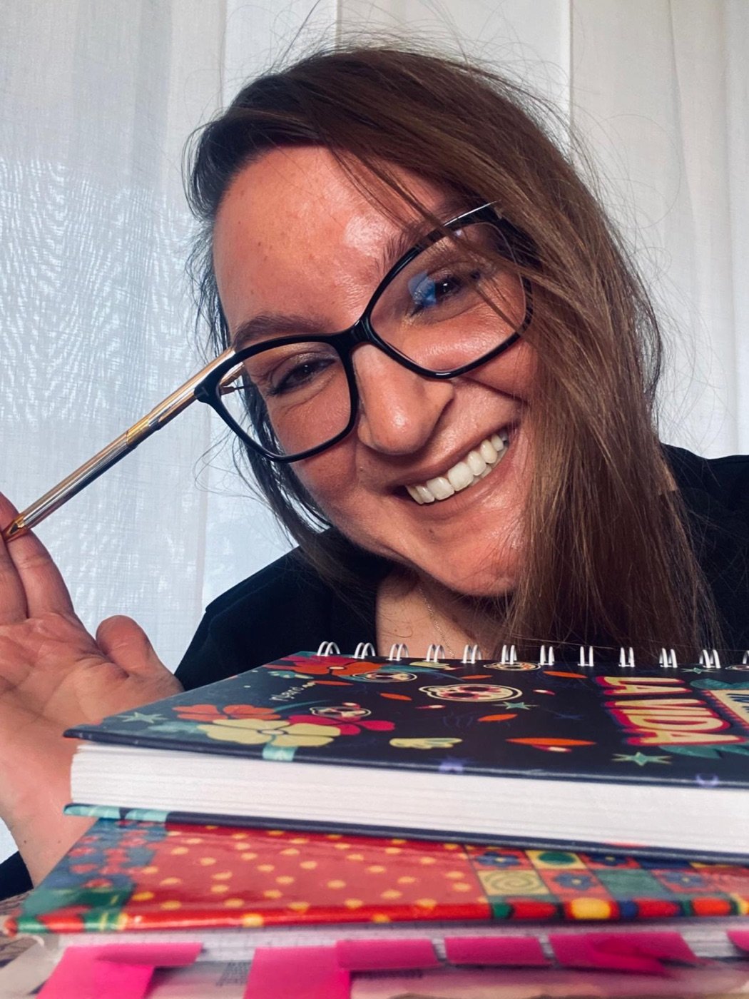 Daniela Linda sorride appoggiata a una pila di quaderni, con una penna in mano.